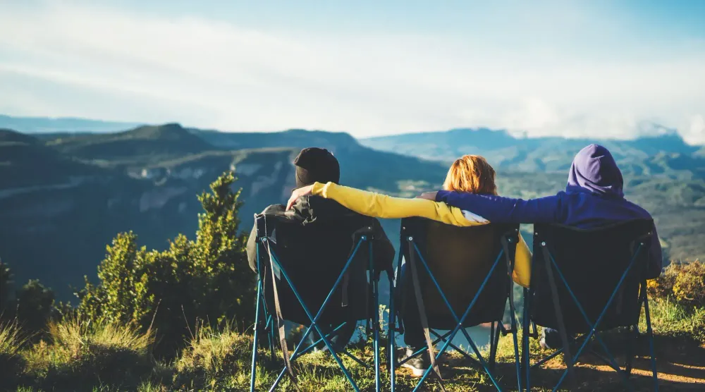 Three friends sitting on camping chairs and looking at a view of the mountains